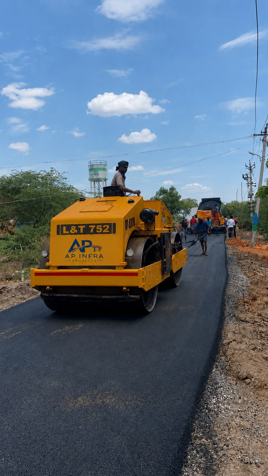 Road roller and paving crew laying bituminous road surface for an AP Infra Projects site